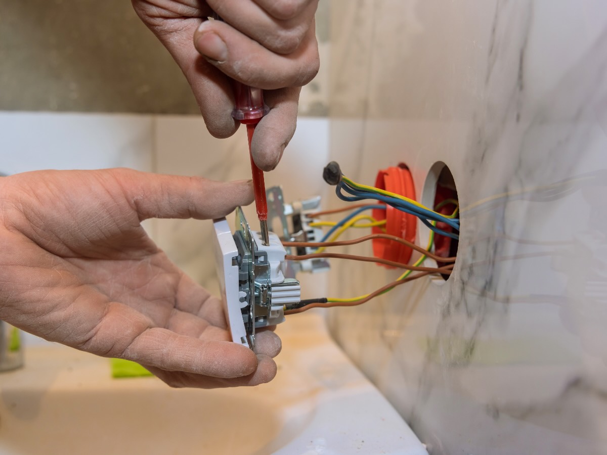 Elektriker schraubt eine Steckdose in eine Dose in einer unverputzten Wand
