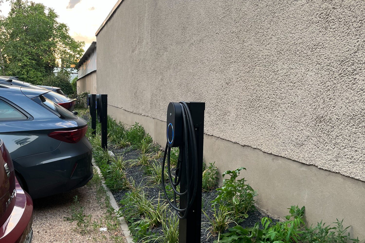 Ladepunkte auf Stelen an einer Hauswand, davor zwei geparkte Autos