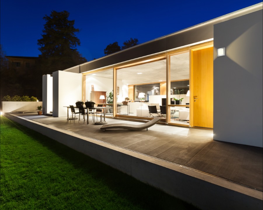 Flachdachhaus am Abend, die Terrasse und der Wohnraum dahinter sind beleuchtet