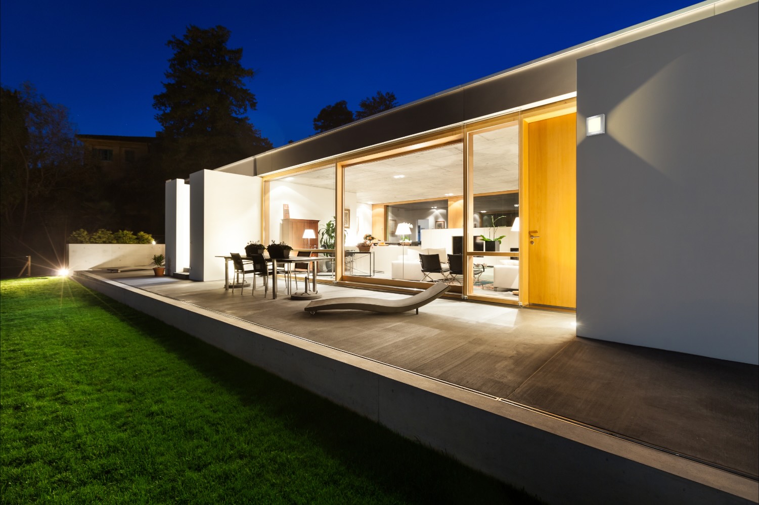 Flachdachhaus am Abend, Terrasse und Garten sind von der Fassade her beleuchtet
