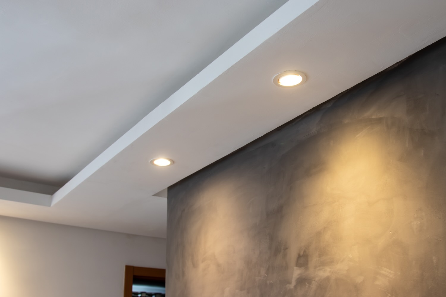 Abgehängte Decke mit Einbauspots, die eine gespachtelte Wand streifend beleuchten
