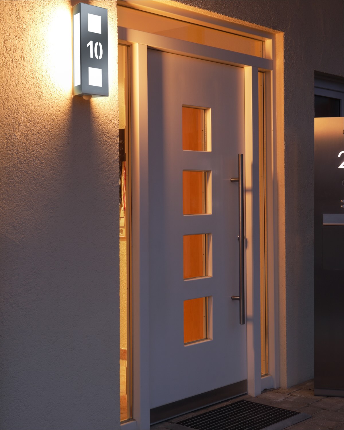 Beleuchteter Hauseingang am Abend, das Licht zeichnet die Stufe vor der Tür nach