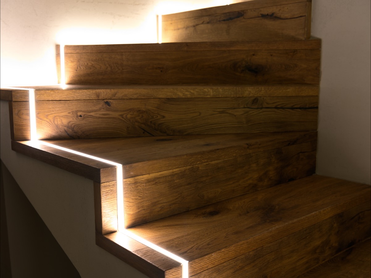 Holztreppe, deren Stufen von eingelassenen Lichtlinien beleuchtet werden
