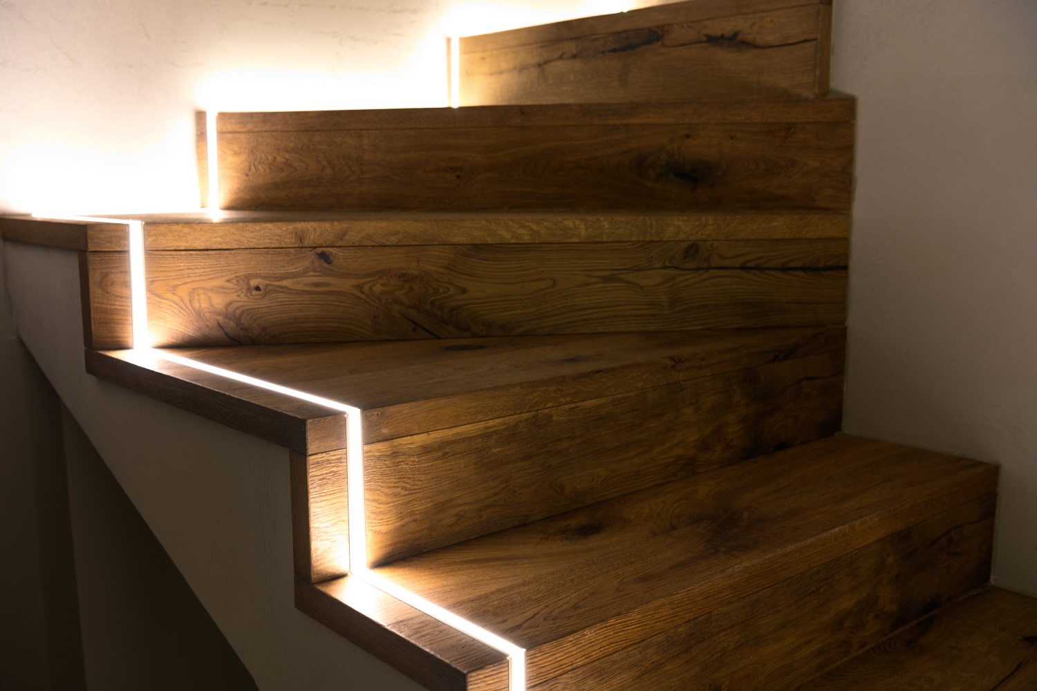 Holztreppe, deren Stufen von seitlich eingelassenen Lichtlinien beleuchtet werden