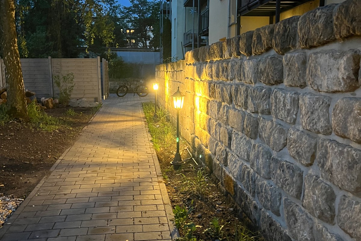 Dieselbe Mauer am Abend, von Bodenstrahlern und Laternen warm angeleuchtet