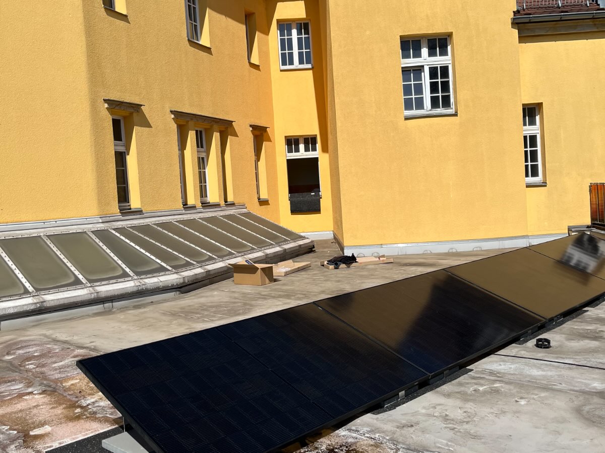 Photovoltaikmodule auf einem Flachdach, dahinter ein Innenhof mit gelber Fassade
