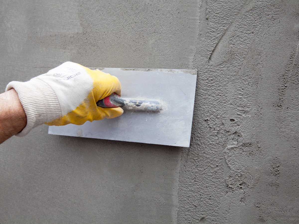 Spachtelmasse wird mit der Glättkelle in dünner Lage auf eine graue Wand aufgezogen