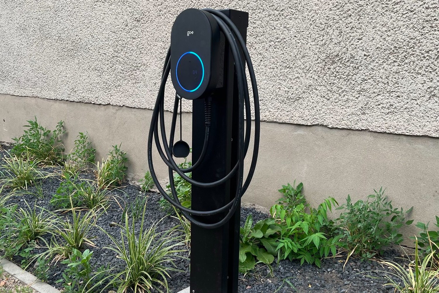 Wallbox auf einer Säule vor einer Hauswand, das Ladekabel hängt aufgerollt am Gerät