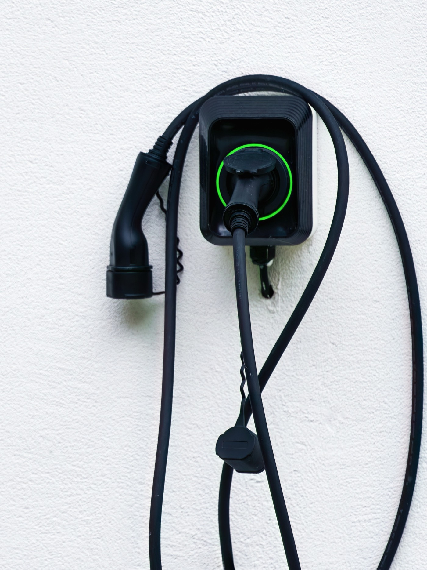 Wallbox an einer hellen Hauswand, das Ladekabel haengt in Schlaufen daneben