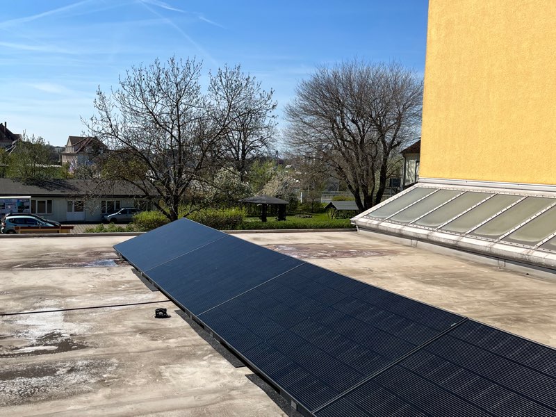 Schräg aufgestellte Photovoltaikmodule auf einem Flachdach vor blauem Himmel