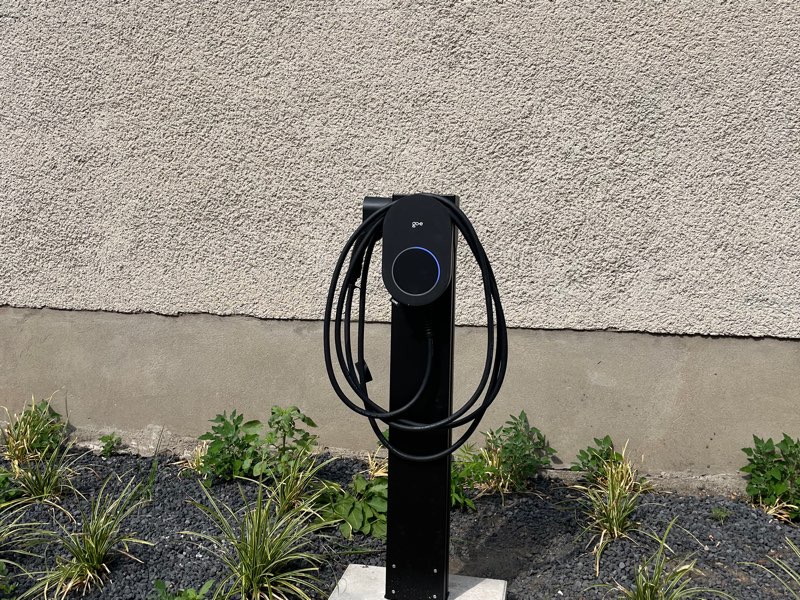 Ladestation auf einer schwarzen Säule mit Betonfundament neben einem Kiesbeet